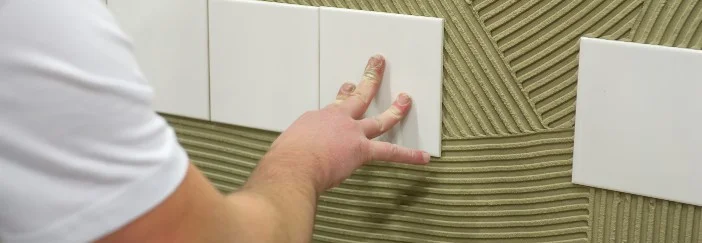 Person bringt Fliese an Wand an